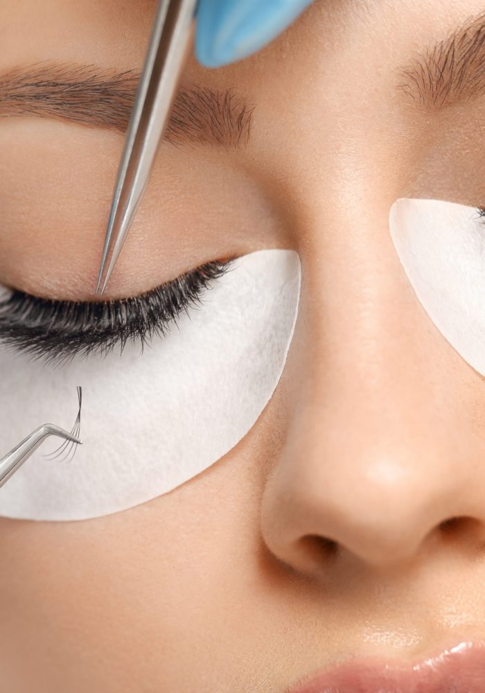 Eyelashes extensions. Fake eyelashes. Eyelash extension procedure.Close up portrait of woman eye with long eyelashes. Professional stylist lengthening female lashes. Master and client in beauty salon.